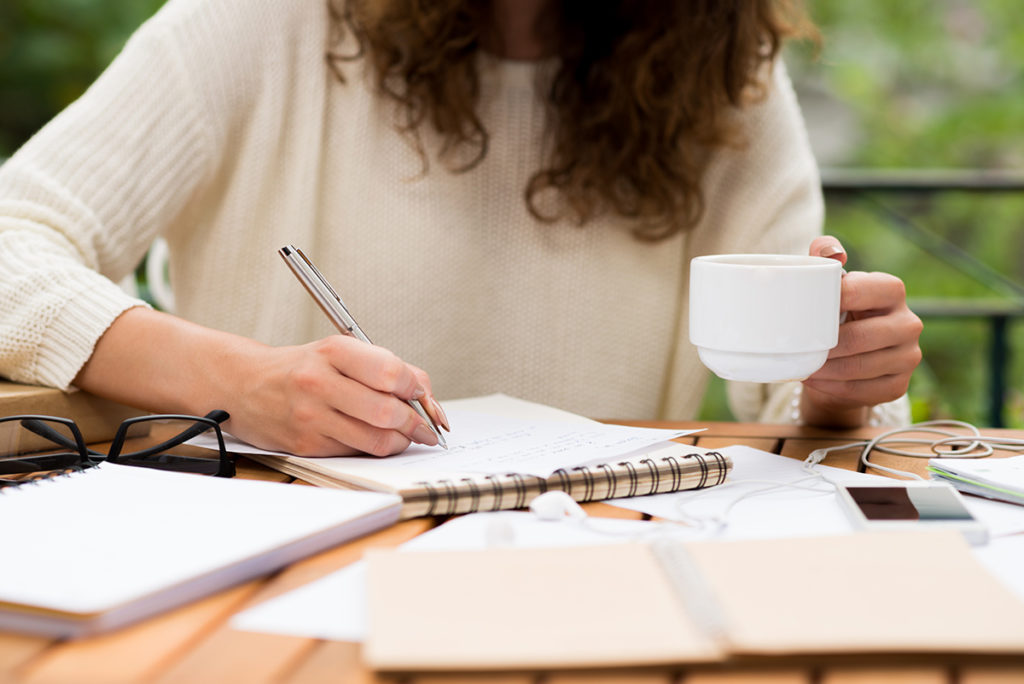 woman with coffee in her hand and an open notebook working on writing ideas