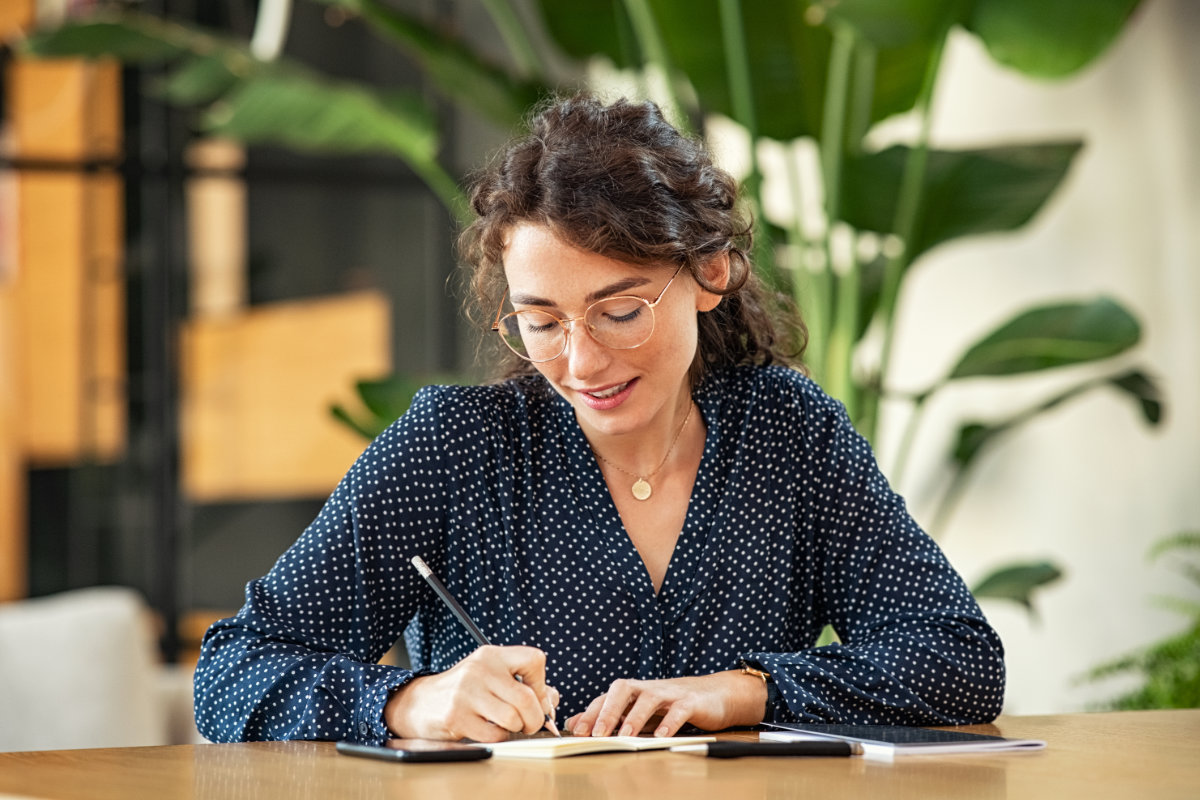 A woman writing in a notebook at a desk, emphasizing the importance of strong written content for effective communication.