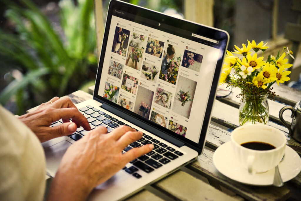 A person browsing a social media platform on a laptop, showcasing various floral arrangements, with a coffee cup and flowers on the table.