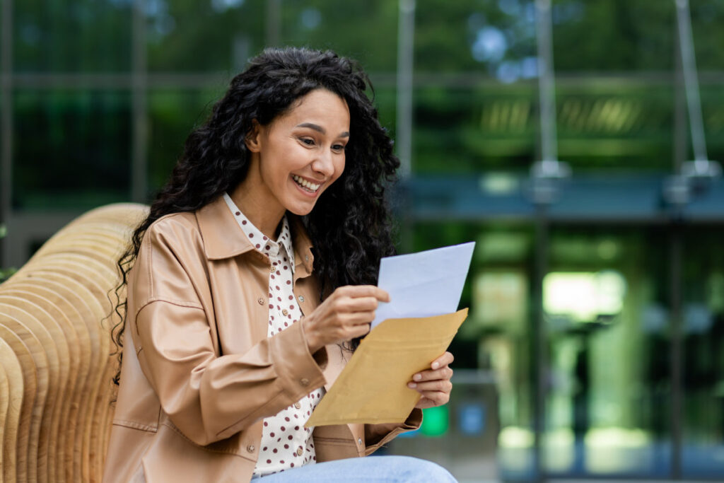 A smiling woman opens an envelope containing a letter, emphasizing the impact of print marketing and direct mail.