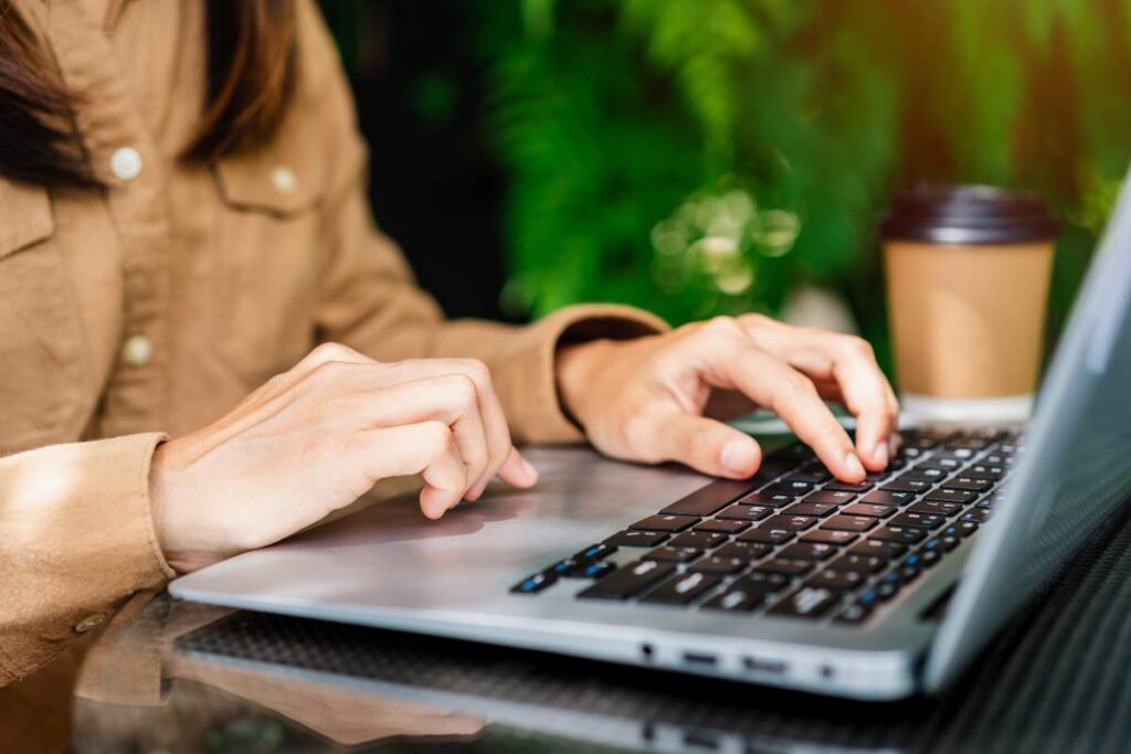 A person typing on a laptop with a coffee cup nearby, symbolizing research on the ideal length of social media posts for effective content strategy.